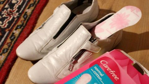 Weiße Schuhe liegen auf einem Holzboden, daneben liegt eine Packung mit Slip-Einlagen für Schwitzfüße im Sommer.