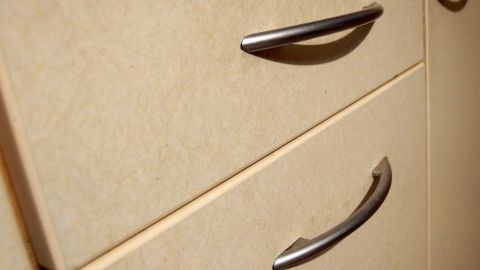 Kunststoffreiniger: Ein supereffektives, günstiges Mittel für hartnäckige Fettschmiere, die sich gerne an Küchenschränken und an den Fliesen über dem Herd ansammelt. Eine Schublade mit Metallgriffen, die für die Beseitigung von Hartnäckiger Fettschmiere geeignet ist, in einem hellen Küchenumfeld.