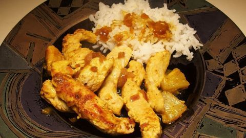 Auf einem Teller liegt eine Putenpfanne mit Ananas und Reis, garniert mit einer süß-sauren Sauce.