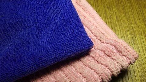 Mikrofaser-Tücher liegen auf einem Holztisch. Sie sind in Blau und Rosa und zeigen die Oberfläche der Stoffe.