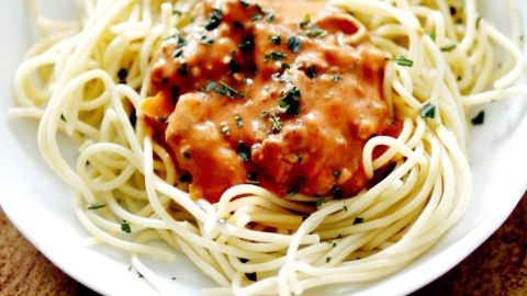 Spaghetti umgeben von einer dicken, cremigen Bolognese-Soße auf einem weißen Teller in einer warmen Umgebung.