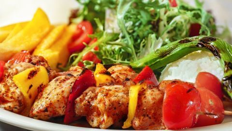 Saftige Backofen-Schaschlik-Spieße liegen auf einem Teller, umgeben von frischem Salat und aromatischen Beilagen.