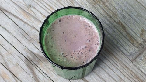 Ein grüner Becher mit einem schaumigen Getränk auf einer rustikalen Holzoberfläche. Abkühler zum Trinken.