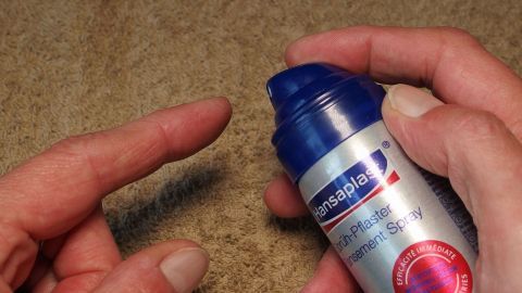 Eine Hand hält eine Flasche mit flüssigem Pflaster, während die andere Hand den Finger mit einer Blase vorbereitet.