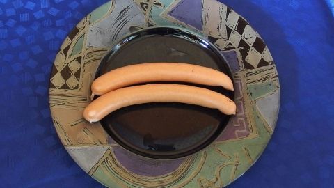 Auf einem bunten Teller liegen zwei Wurststücke. Sie sind ordentlich platziert und heben sich auf dem dunklen Hintergrund ab.