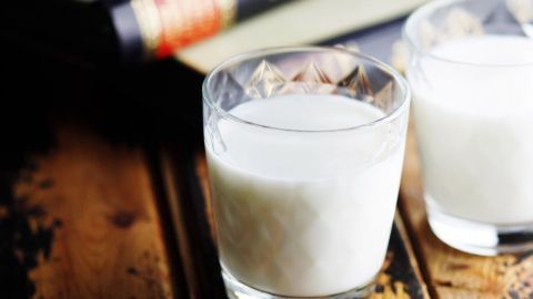 Zwei Gläser mit Milch stehen auf einem rustikalen Holztisch, umgeben von einem dunklen Buch.