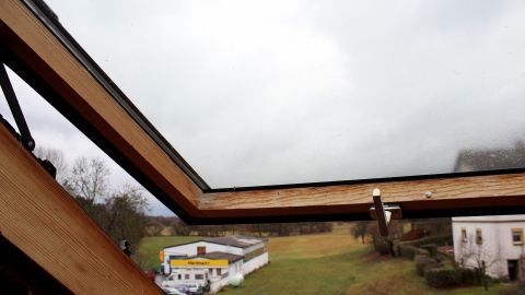Ein geöffnetes Dachfenster blickt auf eine bewölkte Landschaft mit Wiese und Häusern. Scheuermilch könnte hier helfen.