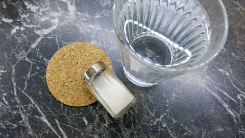 Ein Glas Wasser steht neben einem Korkuntersetzer und einer Salzstreuer, um kurzfristige Schmerzlinderung bei Zahnschmerzen zu fördern.
