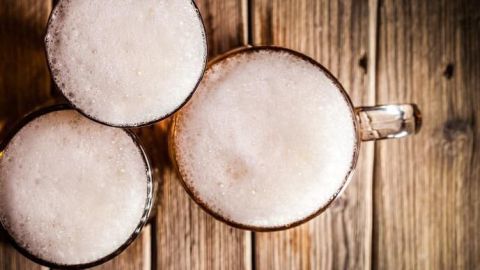Drei Schaumgläser mit Butterbier auf einem rustikalen Holztisch von oben betrachtet.