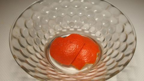Aus den Schalen von Orangen kann man ein duftendes Potpourri herstellen. In einer gläsernen Schale liegt ein runder, orangefarbener Potpourri-Ball auf einem weißen Untergrund und gibt einen frischen Duft ab.