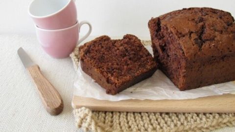 Ein saftiger Nutella-Kuchen steht auf einem Holzteller, neben einer Tasse und einem Messer in einem hellen, gemütlichen Raum.
