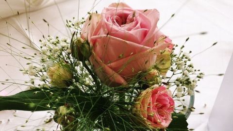 Rosen als dauerhafte edle Tischdekoration - fast für die Ewigkeit - mit Kerzenwachs. Zarte Rosen in einer Vase schmücken einen Tisch, umgeben von filigranen Grün-Elementen, die Eleganz ausstrahlen.