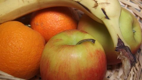 Ein Korb mit frischen Äpfeln, einer Banane und Orangen zeigt Obstvielfalt auf einem Wochenmarkt.