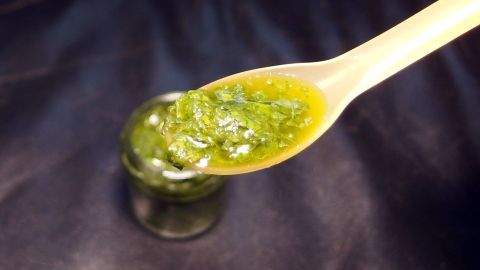 Eine Löffel mit grünem Pesto steht über einem kleinen Glas, während der Hintergrund dunkel gehalten ist, um das Pesto hervorzuheben.