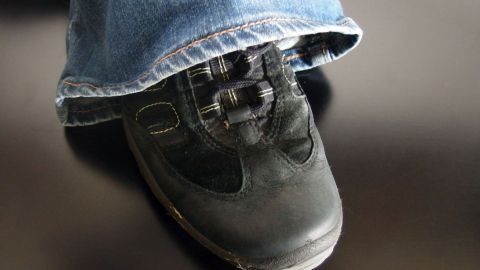 Schwarzer Schuh steht auf einem dunklen Untergrund, während eine Jeans darüber hängt, was eine lässige Alltagsszene zeigt.