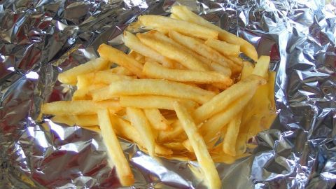 Beschleunige das Backen von Pommes und Kroketten, indem du Alufolie nutzt. Die reflektierende Oberfläche der Folie, wie auf dem Bild gezeigt, sorgt für eine gleichmäßige Hitzeverteilung, die den Backvorgang optimiert. Pommes frites liegen auf Alufolie, bereit zum Backen, in einer Küche.
