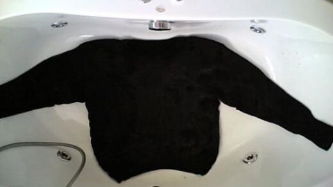 Ein schwarzer Pullover liegt flach in einer Badewanne, um ihn zu dehnen, während er in warmem Wasser eingeweicht wird.