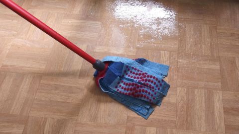 Mit Wasser und Waschpulver Laminat wunderschön sauber bekommen. Ein Wischmopp reinigt glänzend Laminatboden mit Wasser und Waschpulver in einem hellen Raum.