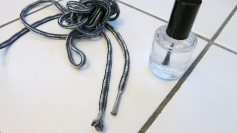 Die Haltbarkeit von Schnürsenkeln mithilfe von Nagellack verlängern. Schnürsenkel liegen neben einem Fläschchen Nagellack auf einem weißen Fliesenboden, um ihre Haltbarkeit zu verlängern.