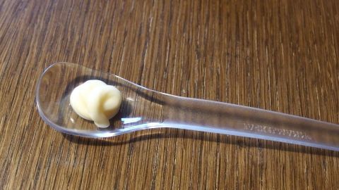 Ein kleiner Löffel mit Mayonnaise liegt auf einem Holztisch, bereit, kleine Brandflecken zu beseitigen.