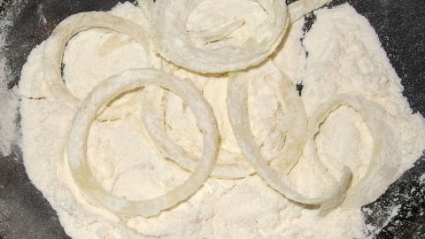 Zwiebelringe liegen in einer Schüssel mit Mehl, bereit zum Frittieren, um knusprig und braun zu werden.