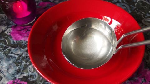 Tipp zum Schmunzeln: Ostfriesische Tomatensuppe - leicht bekömmlich. Eine rote Schale steht auf einem bunten Tisch mit einer silbernen Kelle daneben, bereit für eine ostfriesische Tomatensuppe.