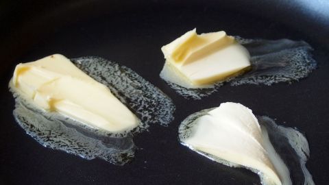 Drei Stücke Butter schmelzen in einer Pfanne, ideal für Backanwendungen oder zum Vergleichen mit Margarine.