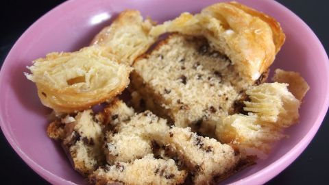 Ein Stück übrig gebliebener Kuchen liegt auf einem pinken Teller, leicht zerbröselt und umgeben von Kuchenteilen.