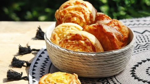 Käse-Taler in einer Schüssel zeigen goldbraune, appetitliche Gebäckstücke auf einem dekorativen Tuch im Freien.