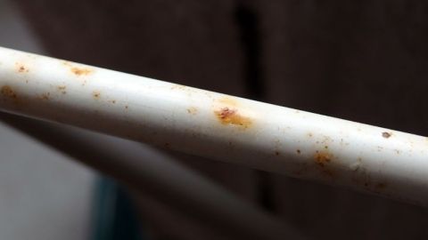 Ein rostiger Metallstab liegt auf einer Oberfläche, sichtbar mit Rostflecken, im Hintergrund unscharf ein Raum.