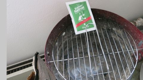 Ein Grillrost liegt auf einem Holzkohlegrill, während eine Packung Natron daneben steht, bereit zur Reinigung.