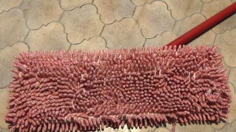Wischmopps nach einigen Malen Wischen gut ausspülen und dann mit in die Waschmaschine geben. Das überstehen sie sehr gut! Ein roter Wischmopp liegt auf einem fliesenartigen Boden, bereit zum Waschen, um für die Reinigung verwendet zu werden.