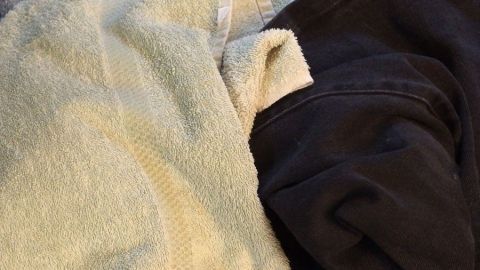 Frische Handtücher und Kleidung liegen übereinander, wirken jedoch muffig, als wären sie nicht richtig getrocknet.