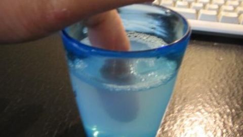 Ein Finger wird in einem Glas mit warmem Seifenwasser eingeweicht, während eine Tastatur im Hintergrund sichtbar ist.