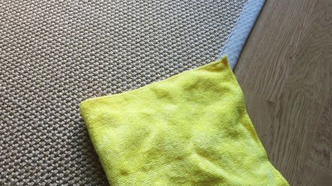 Fast alle Flecken im Teppich können mit einem Mikrofasertuch, Wasser und etwas Spülmittel entfernt werden. Ein gelbes Microfasertuch liegt auf einem Teppich und wird verwendet, um Flecken zu entfernen. Der Teppich ist hell und strukturiert.
