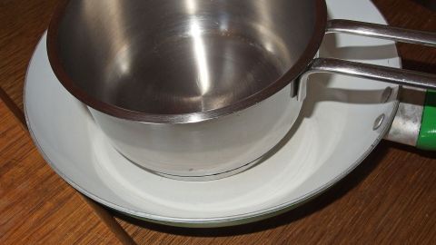 Eine glänzende Edelstahl-Warmhaltekannen steht auf einem weißen Teller, umgeben von einer Holzoberfläche.