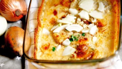 Ein Zwiebel-Sahne-Schnitzel in einer Auflaufform, umgeben von Zwiebeln, frisch gebacken und überbacken.