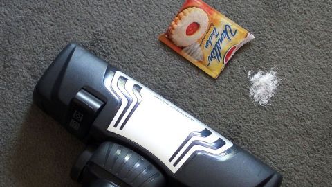 Ein Beutel Vanillezucker oder das preiswertere Vanillinpulver mit dem Staubsauger einsaugen und so duftet es nach jedem Durchgang herrlich nach Vanille. Ein Staubsauger liegt auf einem Teppich neben einer Packung Duftpulver und einem kleinen Haufen weißen Pulvers.