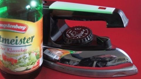 Ein B&uuml;geleisen steht neben einer Flasche Essig auf einem roten Hintergrund, bereit zur Reinigung mit Essig.