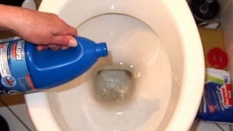 Eine Hand hält eine Flasche Reinigungsmittel und gießt es in eine Toilette, um sie ohne Putzen sauber zu machen.