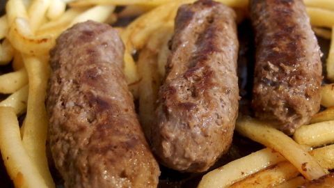 Eine große Menge Hackfleisch gleichmäßig würzen - so gelingt das Vermengen wunderbar. Drei saftige Hackfleischröllchen liegen goldbraun gebraten auf einem Teller neben knusprigen Pommes frites.