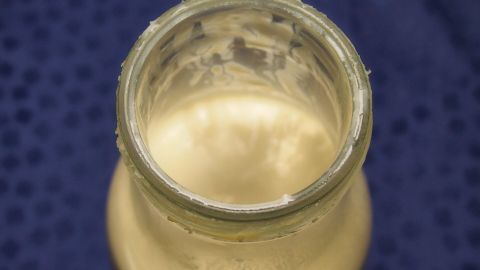 Saure Milch kann man - dank Milchsäure - zum Reinigen der Toilette benutzen. Ein Glas mit saurer Milch steht auf einem blauen Untergrund, bereit zur Verwendung für die Toiletteputzreinigung.