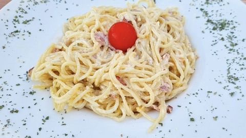 Ein Teller mit Carbonarasoße zeigt cremige Spaghetti, dekoriert mit einer Kirschtomate und frischen Kräutern.