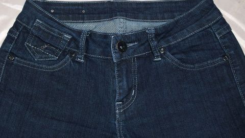 Dunkelblaue Jeans liegen flach auf einem hellen Untergrund und zeigen Bund, Taschen und Schließe, bereit zum Kauf.