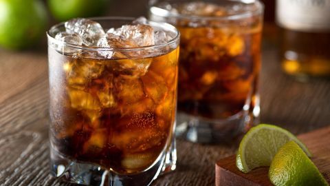 Zwei Gläser Amaretto-Cola stehen auf einem Holztisch, gefüllt mit Eis und einer Limettenscheibe dazu.
