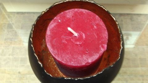 Rote Kerze steht in einem schwarzen Behälter, umgeben von Wachsresten und auf einer glatten Oberfläche, bereit zum Entfernen.