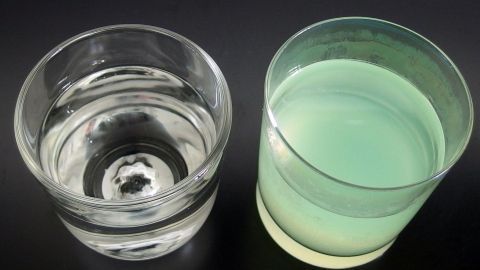 Ein Glas Wasser und ein gefärbtes Getränk stehen nebeneinander auf einem dunklen Hintergrund, bereit zum Trinken gegen Kater.