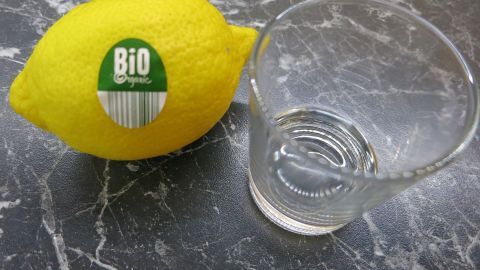 Mit einem vollen Schnapsglas frischgepressten Zitronensaft wirst du Durchfall auf der Stelle los. Eine Bio-Zitrone liegt neben einem leeren Glas auf einer marmorierten Oberfläche, bereit zum Auspressen für Zitronensaft.