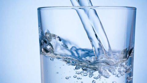 Ein Glas wird mit Salzwasser gefüllt, während Blasen aufsteigen. Der Hintergrund ist hellblau und klar.