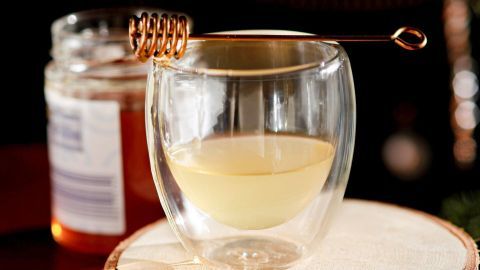 Ein Glas mit Tuxer-Punsch steht auf einem Holzuntersetzer, umgeben von einem Honigglas, in festlicher Umgebung.